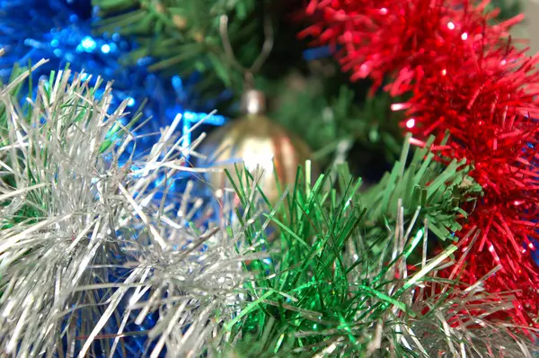 Weihnachtsspielzeug hängt am Weihnachtsbaum, umgeben von buntem Lametta. — Stockfoto