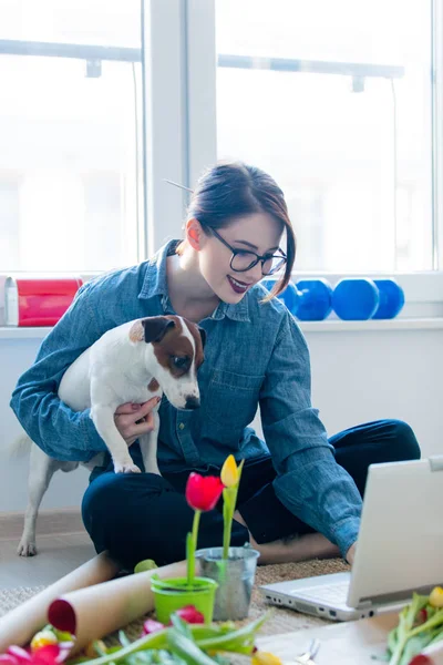 Frau schaut auf Laptop und hält Hund — Stockfoto