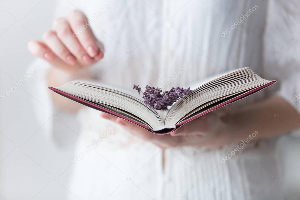 photo of young woman holding opened book with branch of lavender
