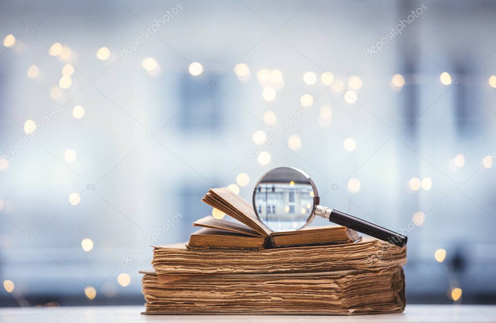 Old books and magnifier on fairy lights