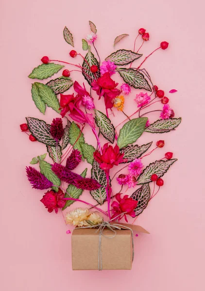 handmade gift box and plant leaves and flowers on pink background