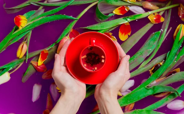 Vrouwelijke Handen Met Kopje Thee Tulpen Paarse Water Achtergrond — Stockfoto