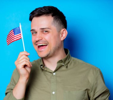 Genç adam bir Amerikan bayrağı mavi arka plan üzerinde tutan