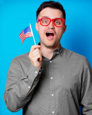 Kırmızı gözlük bir Amerikan bayrağı mavi arka plan üzerinde tutan genç adam