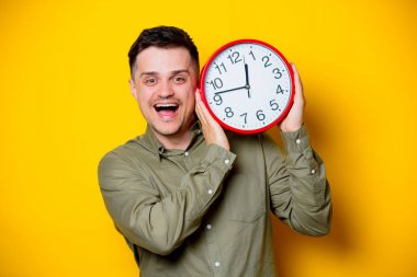 Büyük bir saat tutan bir genç adam. Portre Sarı zemin üzerine