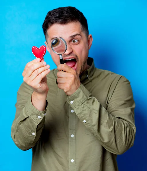 Mladý Překvapený Muž Držící Srdce Lupu Modrém Podkladu — Stock fotografie