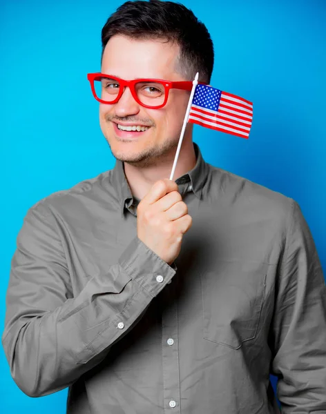 Kırmızı gözlük bir Amerikan bayrağı mavi arka plan üzerinde tutan genç adam
