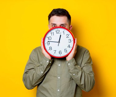 Büyük bir saat tutan bir genç adam. Portre Sarı zemin üzerine