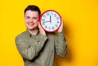 Büyük bir saat tutan bir genç adam. Portre Sarı zemin üzerine