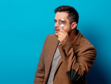 Mavi arka planda büyüteçle şaşırmış bir adam. 