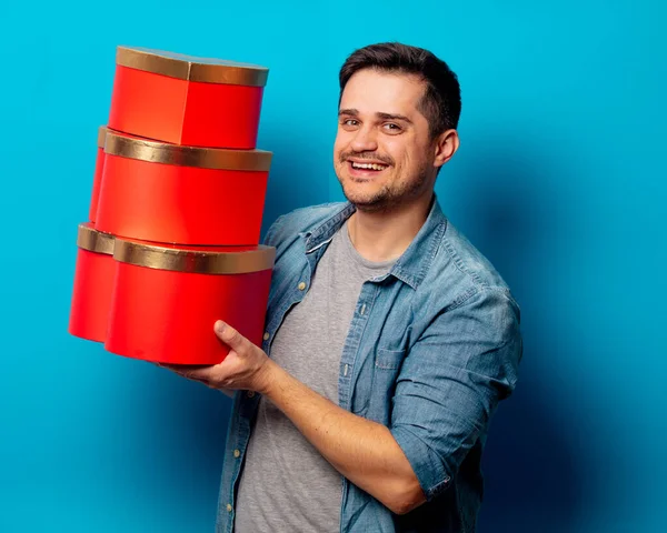 Homem bonito com presentes vermelhos no fundo azul — Fotografia de Stock
