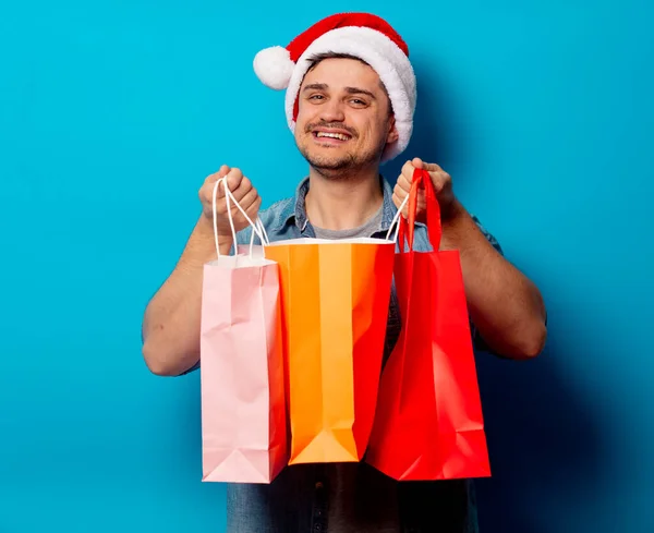 Snygg man i julhatt med shoppingväskor på blå bakgrund — Stockfoto