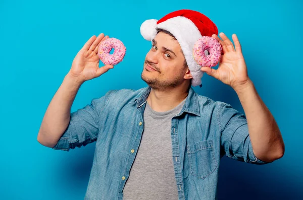Knappe man in kerstmuts met donuts op blauwe achtergrond — Stockfoto