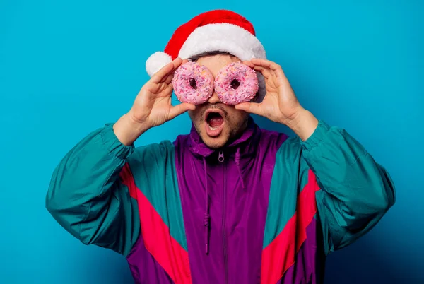 Knappe man met kerstmuts en jaren '90 jasje met donuts op blauw — Stockfoto