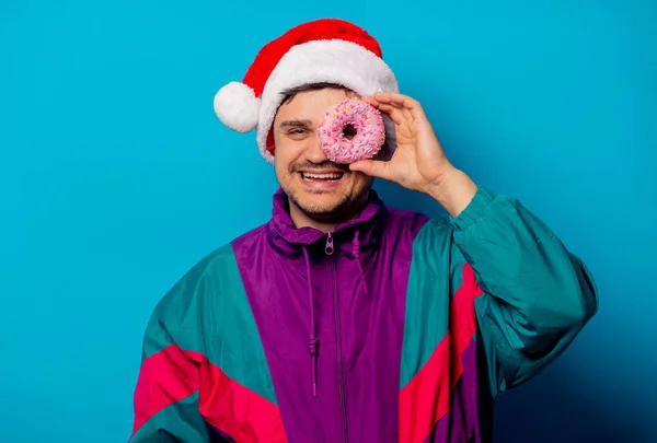 Bonito homem de chapéu de Natal e casaco dos anos 90 com donut em azul — Fotografia de Stock