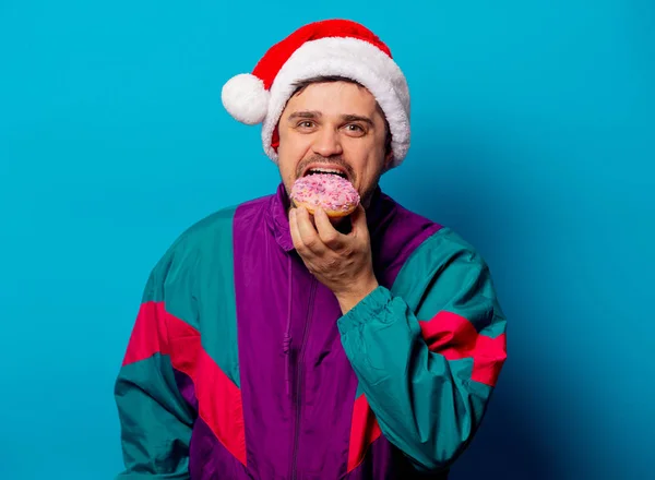 Knappe man met kerstmuts en jaren '90 jasje met donut op blauw — Stockfoto