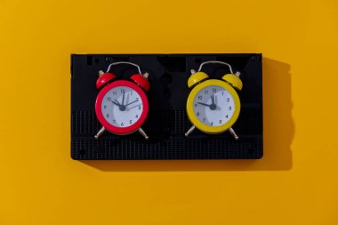 Two vintage alarm clocks and VHS cassette on yellow background clipart