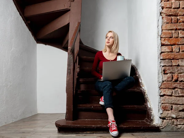 Hipster rubia con ordenador portátil se sienta en las escaleras de edad en c edad — Foto de Stock