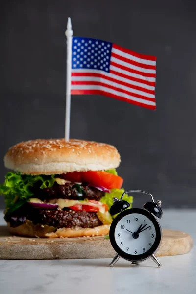 Beef burger with USA flag on tray and alarm clock