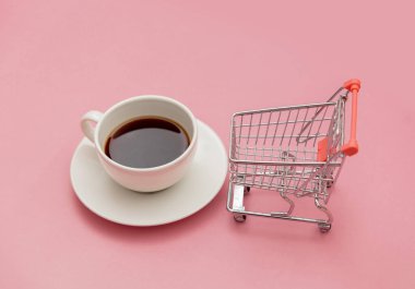Bir fincan kahve ve alışveriş arabası pembe renkli masada.