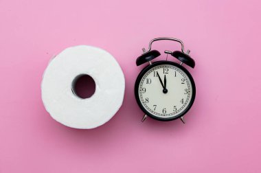 Pembe arka planda tuvalet kağıdı ve alarm saati