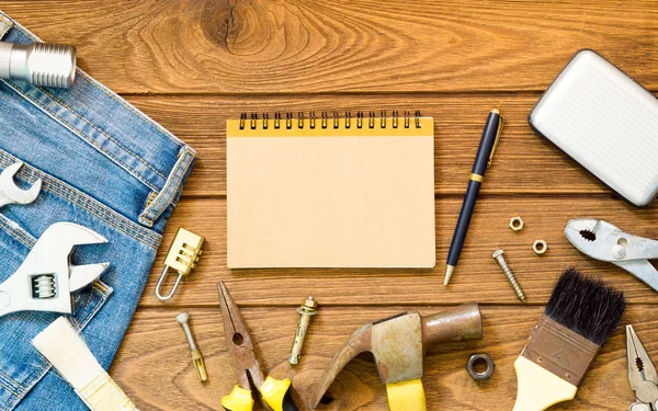 Jeans and many handy tools, blank space notebook on wooden backg