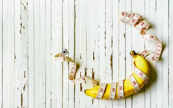 Dieta conceito saudável. Banana com fita métrica em madeira branca — Fotografia de Stock