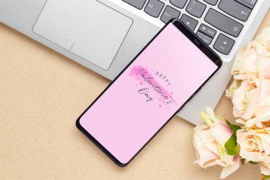 Bilgisayar dizüstü bilgisayarında akıllı telefon ve atölyede gül çiçeği.