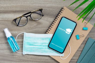 Evde hashtag, pandemik koronavirüs önleme kampanyası konsepti. Maskeli bir model cep telefonu ve ofis masasında Alkol Mini El dezenfektanı..