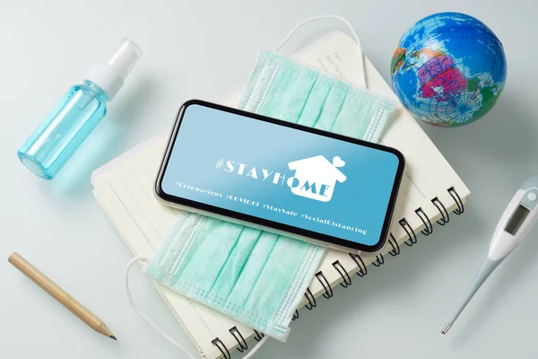 Evde hashtag, pandemik koronavirüs önleme kampanyası konsepti. Maskeli bir model cep telefonu ve ofis masasında Alkol Mini El dezenfektanı..