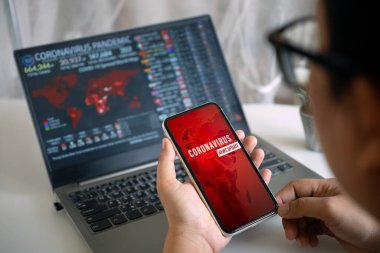 Coronavirus ya da Covid-19 salgın haber güncelleme arka plan kavramı. Mockup cep telefonu, akıllı foe tutan ve Covid 19 salgını için laptop ekranına bakan biri..