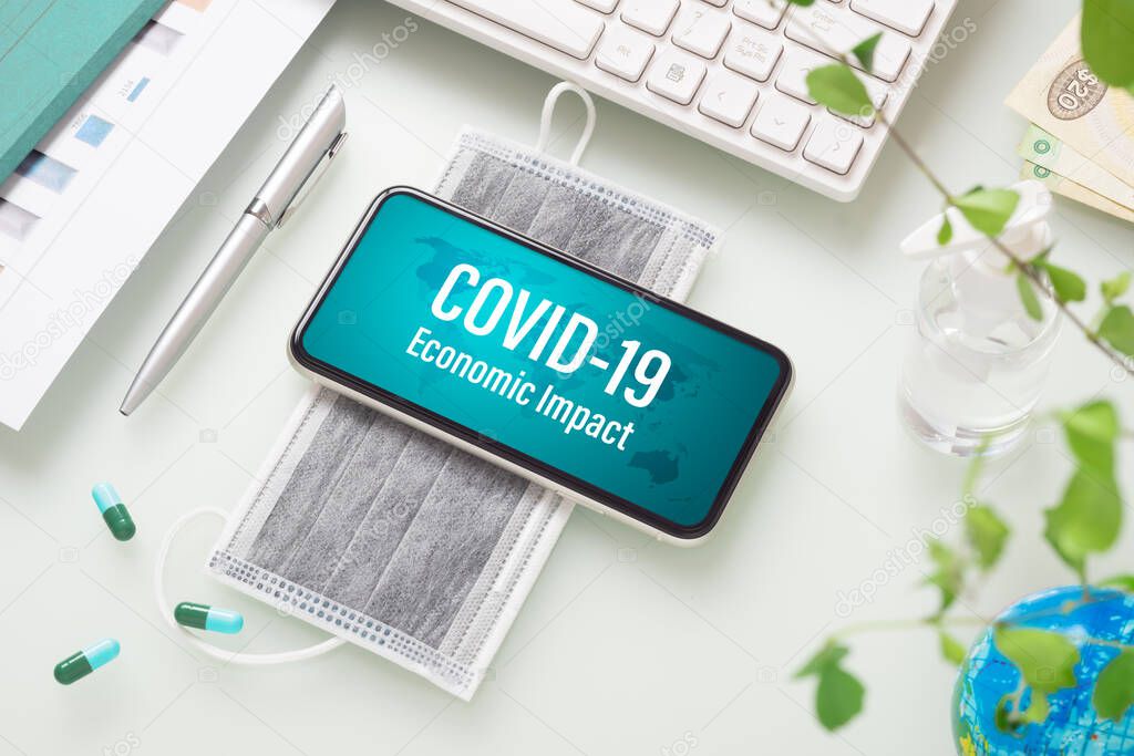 COVID-19 or Corona virus ECONOMIC IMPACT background concept. Mockup mobile phone for Covid 19 business impact with facial masks and Alcohol Mini Hand Sanitizer gel on working office desk table workspace.