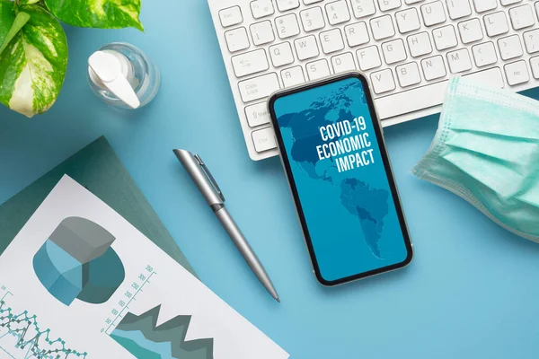 Coronavirus Covid-19 salgını ekonomik etki arka planı kavramı. Bilgisayar klavyesi, iş grafikleri, yüz maskesi ve el dezenfektanı olan Mockup cep telefonu, covid 19 iş riski için çalışma masasında..