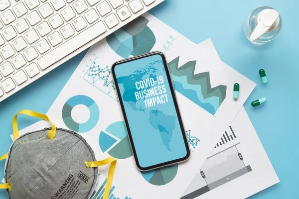 Coronavirus Covid-19 salgın hastalık salgını iş hayatını etkiledi. Bilgisayar klavyesi, iş grafikleri, yüz maskesi ve el dezenfektanı olan Mockup cep telefonu, covid 19 iş riski için çalışma masasında..