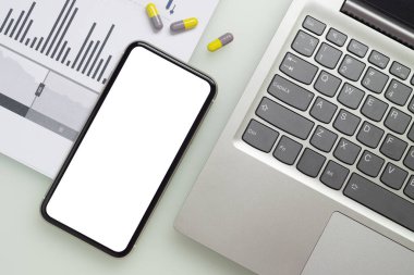 Coperid-19 Coronavirus iş krizi arka plan konsepti için çalışma masasına dizüstü bilgisayarı, iş çizelgesi ve tıbbi tabletleri olan boş ekran cep telefonu modeli..