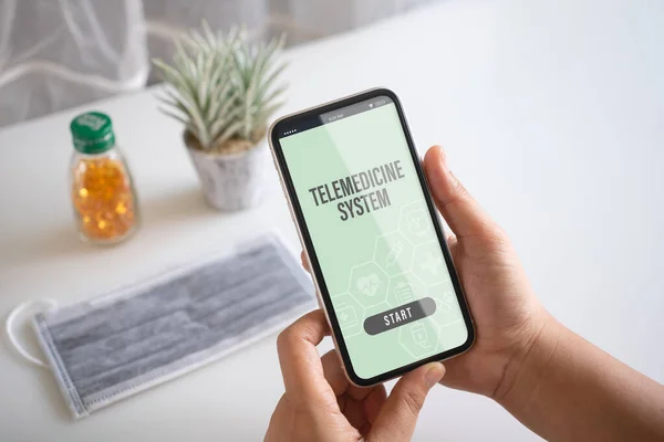 Telemedicine online application background concept. Mockup mobile phone, a person holding smartphone using the telemedicine system application with facemask and medical on table.