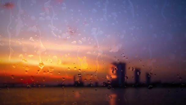 雨が川の町の上にガラスに落ちる 日没の間に雨の下で都市と川を焼き ガラス窓に雨が降りました — ストック動画