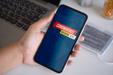 Coronavirus veya Covid-19 salgını Son Dakika Haberleri arka plan konsepti. Mockup cep telefonu, elinde Coronavirus virüslü akıllı bir kişi cep telefonundan flaş haber veriyor..