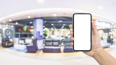 Bulanık mobilya mağazası arka planına sahip beyaz ekran akıllı telefon modeli. Mobilyaların çevrimiçi alışverişi için cep telefonunu taklit et.