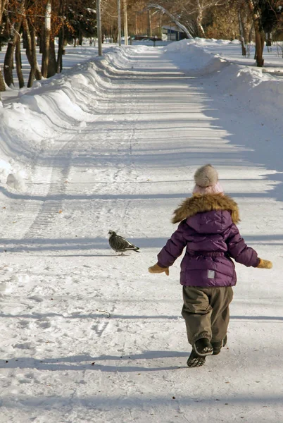 Παιδί σε λιλά χειμωνιάτικα ρούχα τρέχει στο χιόνι χειμερινό πάρκο — Φωτογραφία Αρχείου