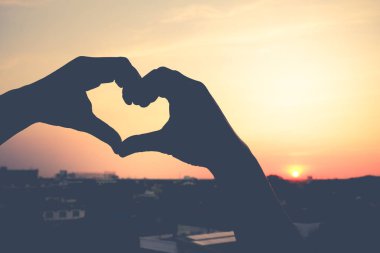 bir kalp sembolü bir günbatımı gökyüzü üzerinde tutan bir el silüeti