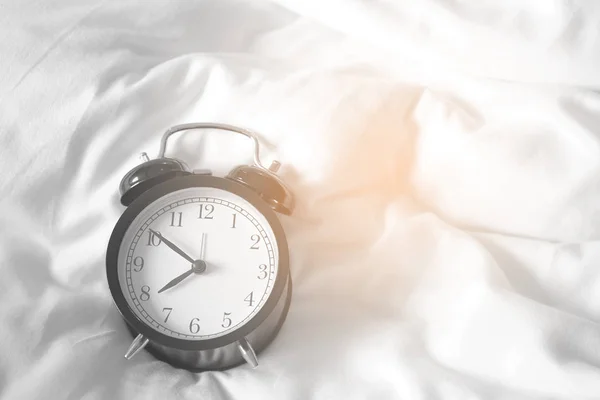 Reloj despertador de estilo negro vintage lugar en una cama de color blanco . —  Fotos de Stock