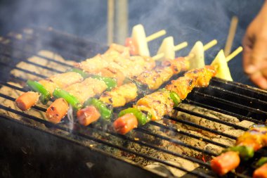 Mangal kömürü ocağında kızartılıyor ve gece pazarında duman yüzüyor..