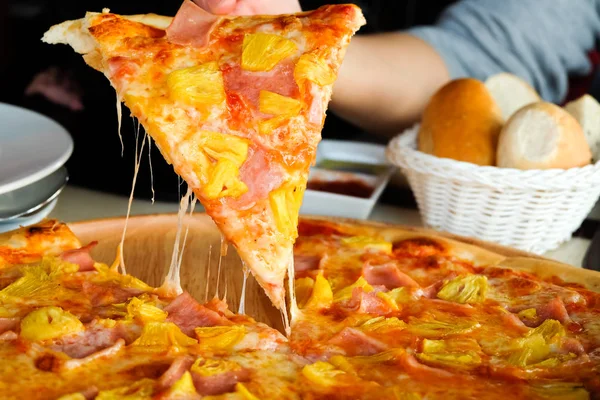 Close up Woman\'s hand picked Hawaiian pizza from a wooden tray on the table.