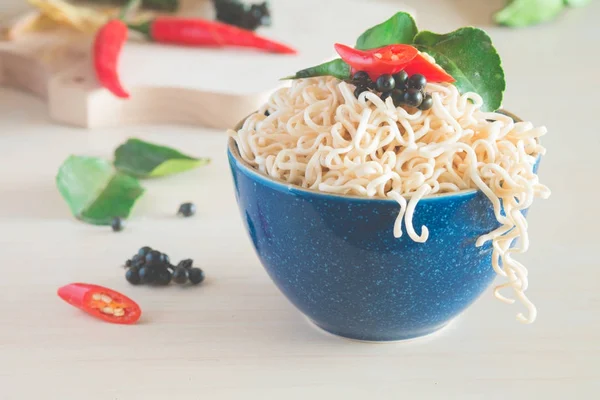 Instant noodles in a bowl with chili pepper and lime leaves on old wooden table — Stock Photo, Image