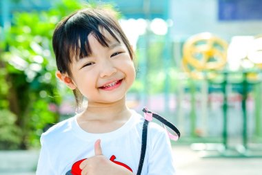 Asyalı çocuk kız başparmak yukarı ve parlak mutluluk Park ile gülümseyen