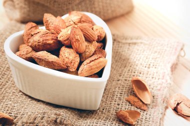 Yas ve ahşap zemin üzerinde bir kalp şekilli kasede kabuğundaki badem fındık.