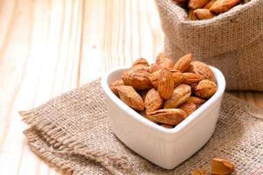 Yas ve ahşap zemin üzerinde bir kalp şekilli kasede kabuğundaki badem fındık.