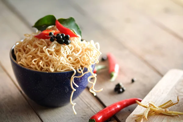 Instant noodles in a bowl with chili pepper and lime leaves on old wooden table