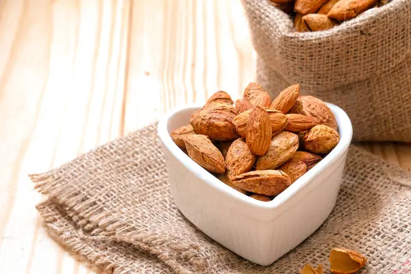 Yas ve ahşap zemin üzerinde bir kalp şekilli kasede kabuğundaki badem fındık.